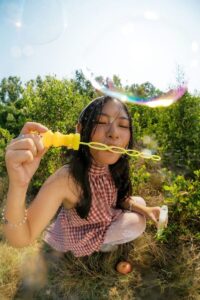 Young woman in checkered dress blowing bubbles outdoors.